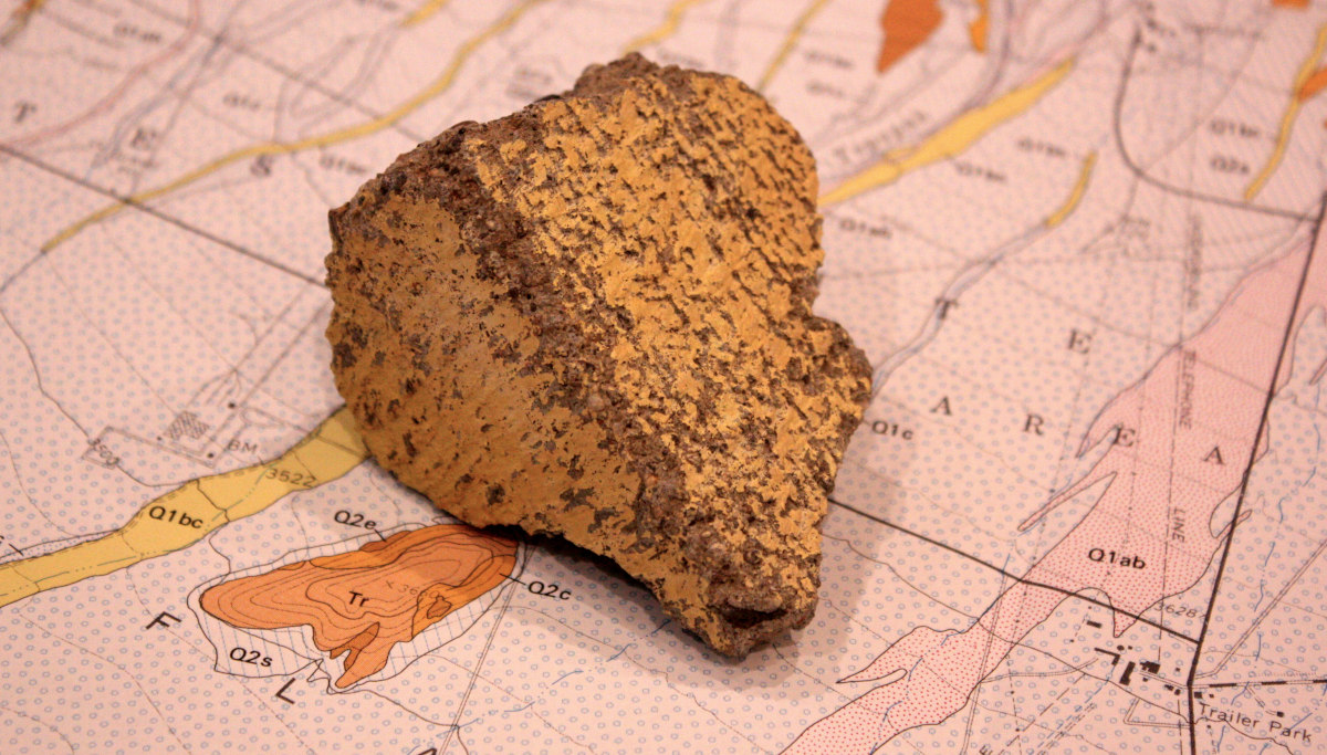A small piece of concrete, painted yellow on two sides, sitting on top of a geologic map.